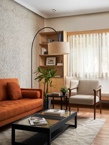 Living room corner with orange sofa, wood shelving unit, arc lamp, and sheer-curtained window