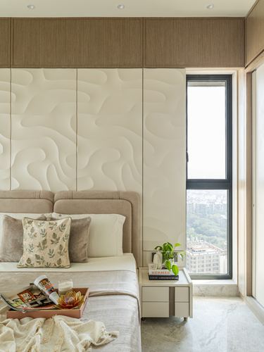 High-rise bedroom with textured wall panel, beige headboard, and city view through tall window