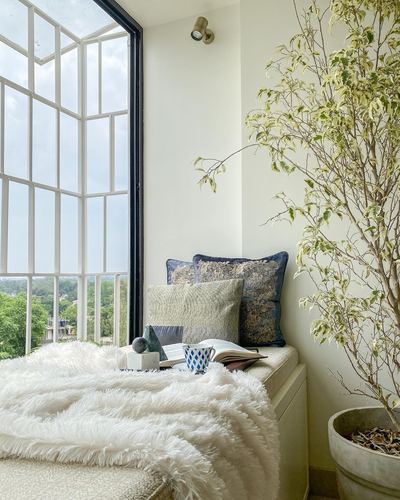 Window seat with fluffy throw and patterned pillows beside a tall crittall-style window and potted tree