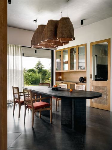 Dining area with oval stone table, cane chairs, and clustered woven pendant lamps overlooking garden