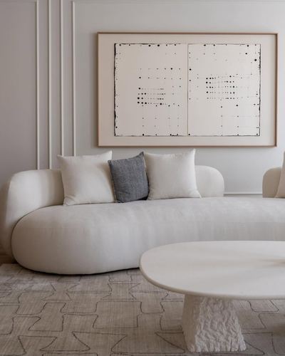 Curved cream boucle sofa beneath framed abstract art, sculptural pedestal coffee table on patterned rug