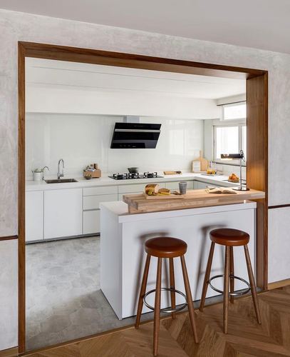 White kitchen with island, wood counter overhang, and two leather-top bar stools seen through a timber-framed doorway