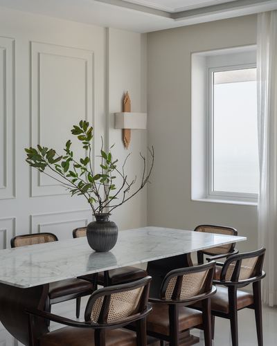 White dining room with marble table, cane chairs, and a sculptural vase of branches
