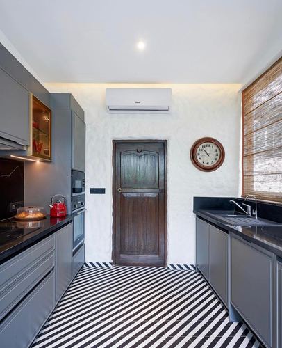 Grey galley kitchen with striped floor, wooden door, round clock, and cane blind