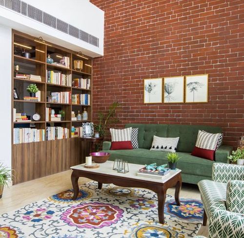 Living room with green tufted sofa, brick wall, wooden bookshelf and colorful medallion rug