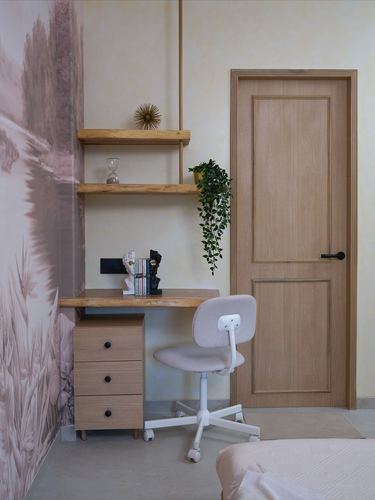 Small study corner with floating wood shelves, desk, pink chair, and wood door beside a mural wall