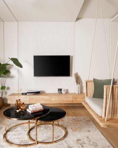 Living room with fluted white wall, mounted TV, wood console, and hanging rattan swing chair
