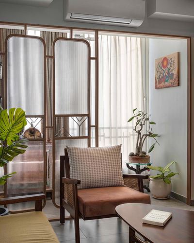 Living room corner with cane armchair, wood-framed fluted glass divider, and potted plants