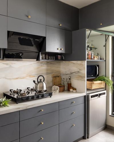 Charcoal grey modular kitchen with marble-look backsplash, brass knobs, and gas stove with kettle