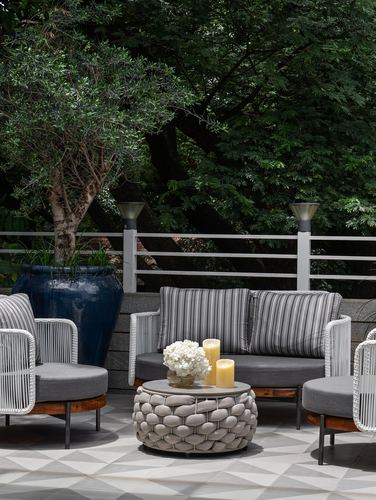 Outdoor terrace seating with woven chairs, striped cushions, and a green tree backdrop