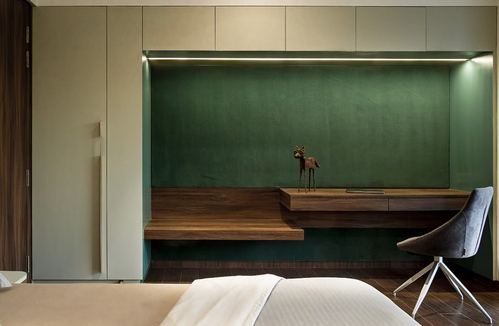 Bedroom with green niche wall, floating wood desk, brass deer figure, and grey swivel chair