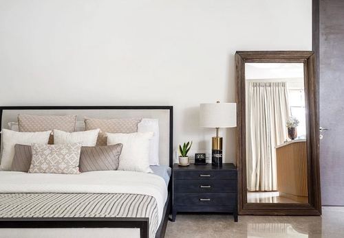 Neutral bedroom with upholstered bed, dark wood nightstand, brass lamp, and large leaning mirror