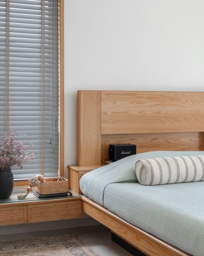 Wooden bed with sage green linens beside a cane-front nightstand and venetian blinds