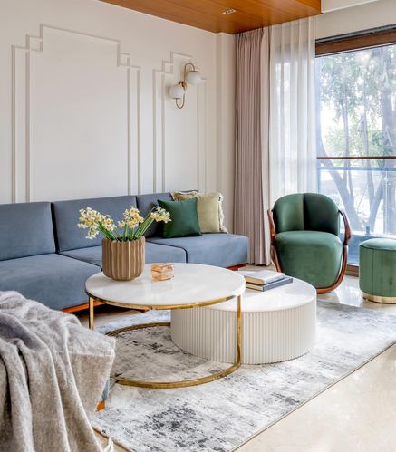 Living room with blue sectional, green velvet chair, and nested round marble coffee tables by a window