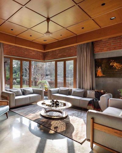 Living room with brick walls, wood coffered ceiling, corner glass doors, and grey sofas around a round table