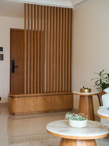 Entry foyer with vertical walnut slat screen, matching door, and round marble-top side tables