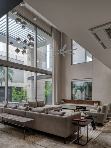 Double-height living room with floor-to-ceiling glass wall, cube chandelier, sectional sofa and view to garden