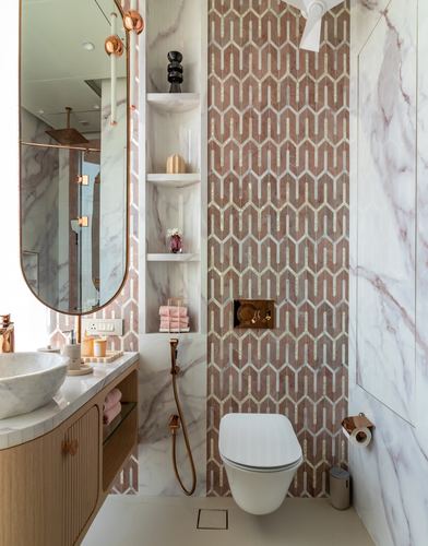 Bathroom with veined stone walls, rose gold fixtures, and a pink chevron mosaic accent wall behind the toilet