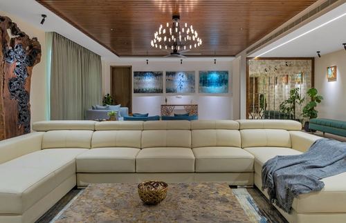 Large living room with cream leather sectional, wood ceiling, chandelier and carved tree sculpture