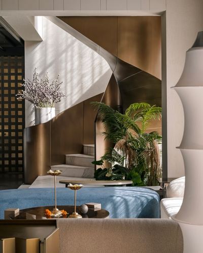 Living room with blue ottoman facing a sculptural bronze-clad staircase and marble steps