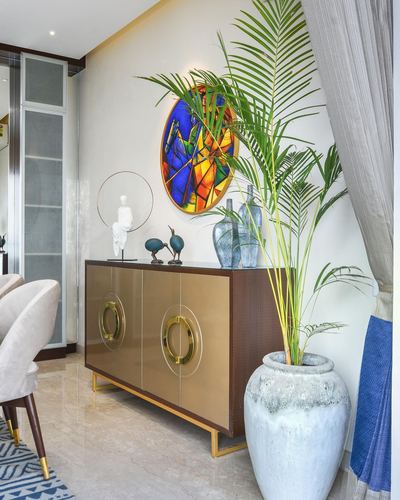 Entryway sideboard with brass ring handles, round colorful glass art, and large potted palm