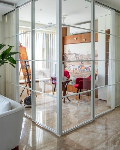 Glass-framed partition looking into a study with red velvet chairs and mural, marble floor
