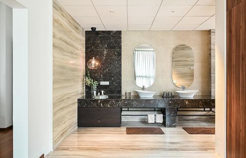 Double vanity bathroom with dark stone wall, oval mirrors, and light wood-grain walls