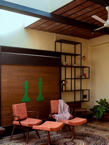 Living room with brick ceiling, walnut wall with green chess motifs, and coral chairs