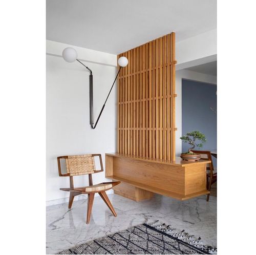 Wood slat partition with floating bench, cane chair, and bonsai in a bright foyer