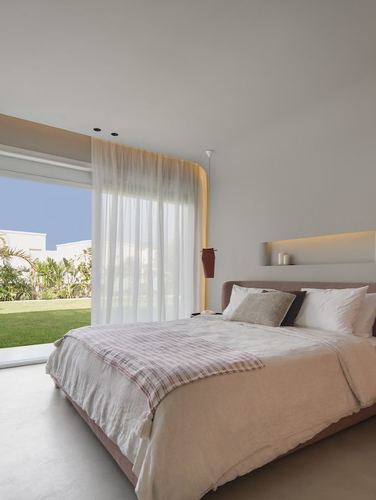 Minimalist bedroom with curved blush headboard, sheer curtains, and glass door opening to green lawn