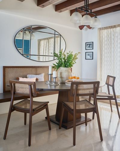 Dining table with cane chairs beneath oval mirror and exposed wood beam ceiling