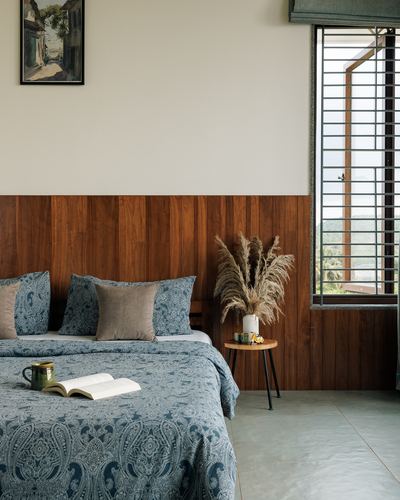 Bedroom with wood-paneled wall, blue paisley bedding, pampas grass, and tall louvered window