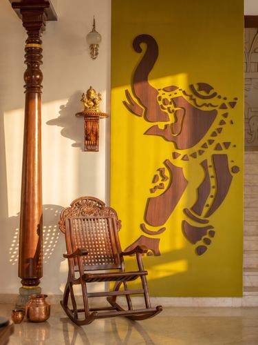 Carved wooden rocking chair beside a mustard wall with an elephant motif cut-out and turned pillar