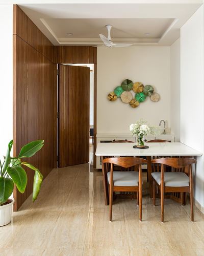 Dining area with wood pivot door, marble table, and circular metal wall art