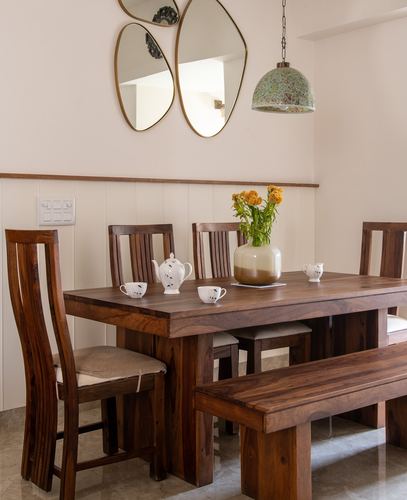 Wooden dining table set with teapot and flowers under a mosaic pendant light, mirrors above wainscot wall