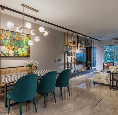 Open-plan dining and living room with teal velvet chairs, brass chandelier and marble floor