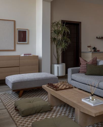 Japandi living room with wood coffee table, grey sofa, olive cushions and a tall potted plant near a dark wood door