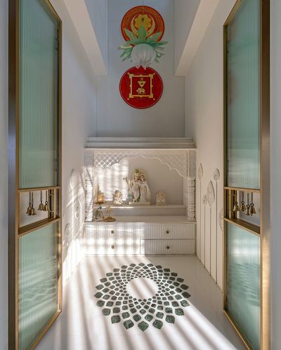 Narrow white marble pooja room with carved altar, brass bells, and green mosaic floor medallion