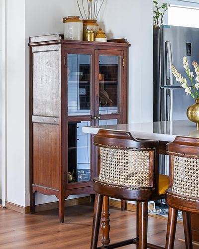 Vintage wooden glass-front cabinet with ceramic jars beside cane bar stools and kitchen counter
