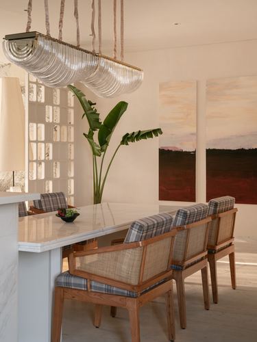 Marble dining table with cane chairs beneath a glass chandelier, sunset diptych on wall