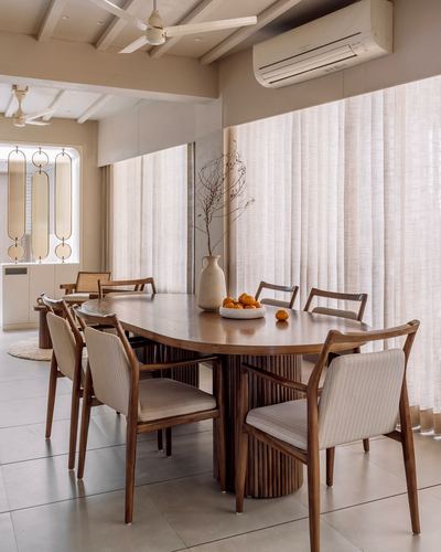 Oval wood dining table with fluted base, cane-back chairs, sheer curtains and ceiling fan