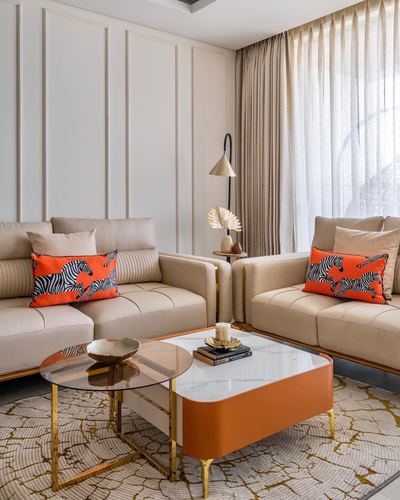 Beige living room with two sofas, zebra print cushions, and an orange lacquered coffee table beside a round glass one