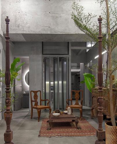 Concrete living space with carved wooden poles, cane chairs and a striped rug