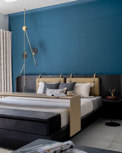 Bedroom with teal wall, dark wood bed, tan leather headboard and sculptural brass pendant light