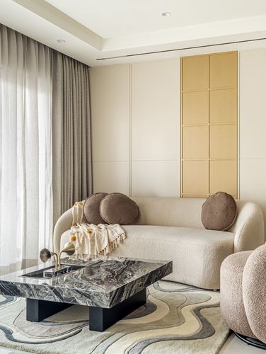 Curved beige boucle sofa beside marble coffee table with swirl-patterned rug