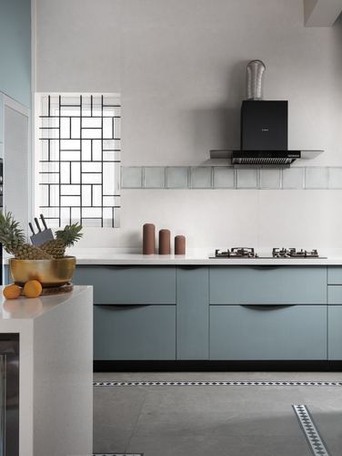 Dusty blue kitchen cabinetry under white countertop with black chimney hood and patterned window grille