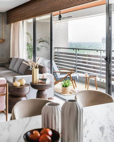 Living room with grey sofa, wood side tables and marble table opening onto a balcony with city view