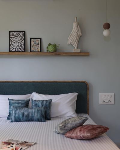 Bedroom corner with curved teal headboard, floating shelf with art and sculpture, layered pillows