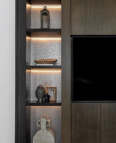 Dark wood built-in shelving with backlit stone texture, decorative objects, and a mounted tv
