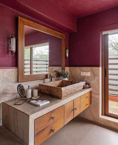 Maroon bathroom with wood-framed mirror above a carved stone sink on a floating wooden vanity